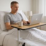 Man in a hospital bed, using an overbed table to work on his laptop