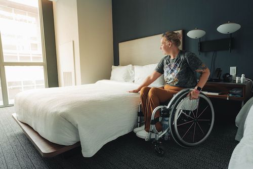 A young women in a wheelchair tests access to an hotel bed where she is staying
