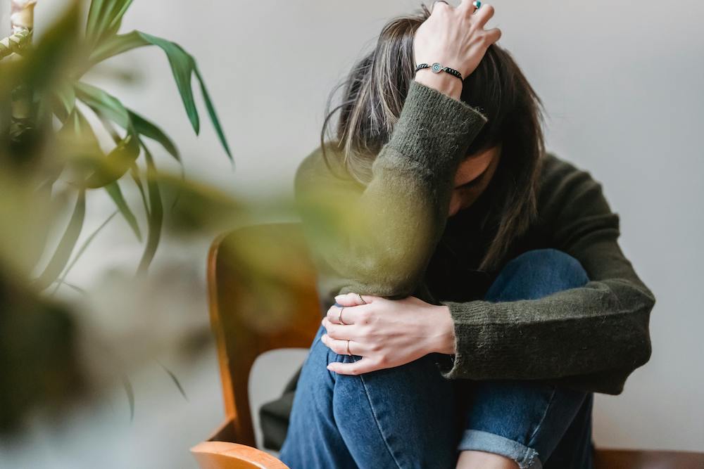 A girl sits on a chair with her head on her knees