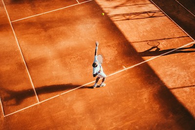 A young man plays tennis on a clay court